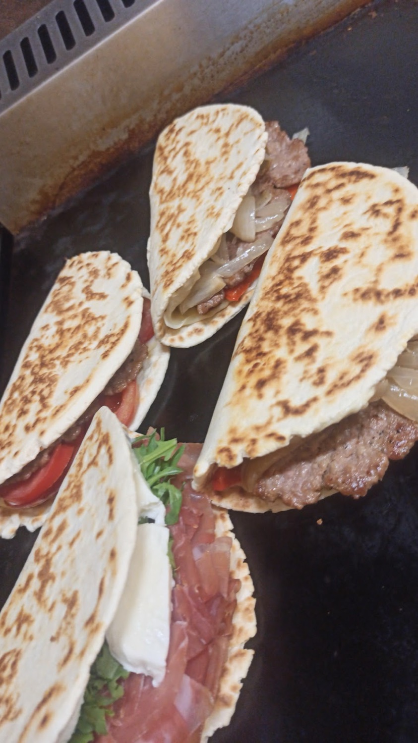 Piadine appena farcite con salsiccia, cipolla e crudo sulla piastra